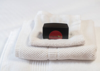 A box of Chocolatea chocolates on top of folded towels on a bed.